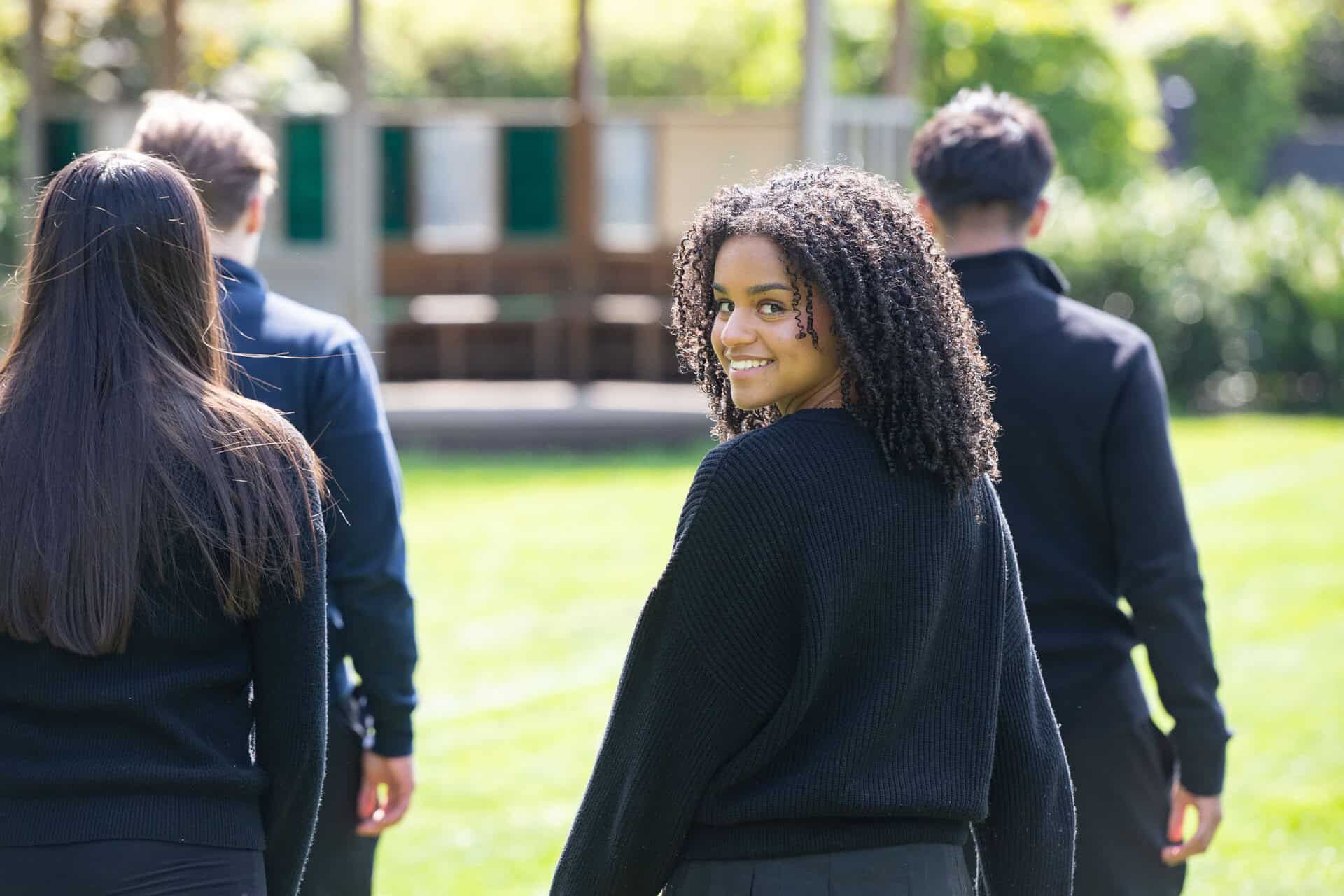 A smiling Thorpe House Sixth Form student walking with friends across the school field